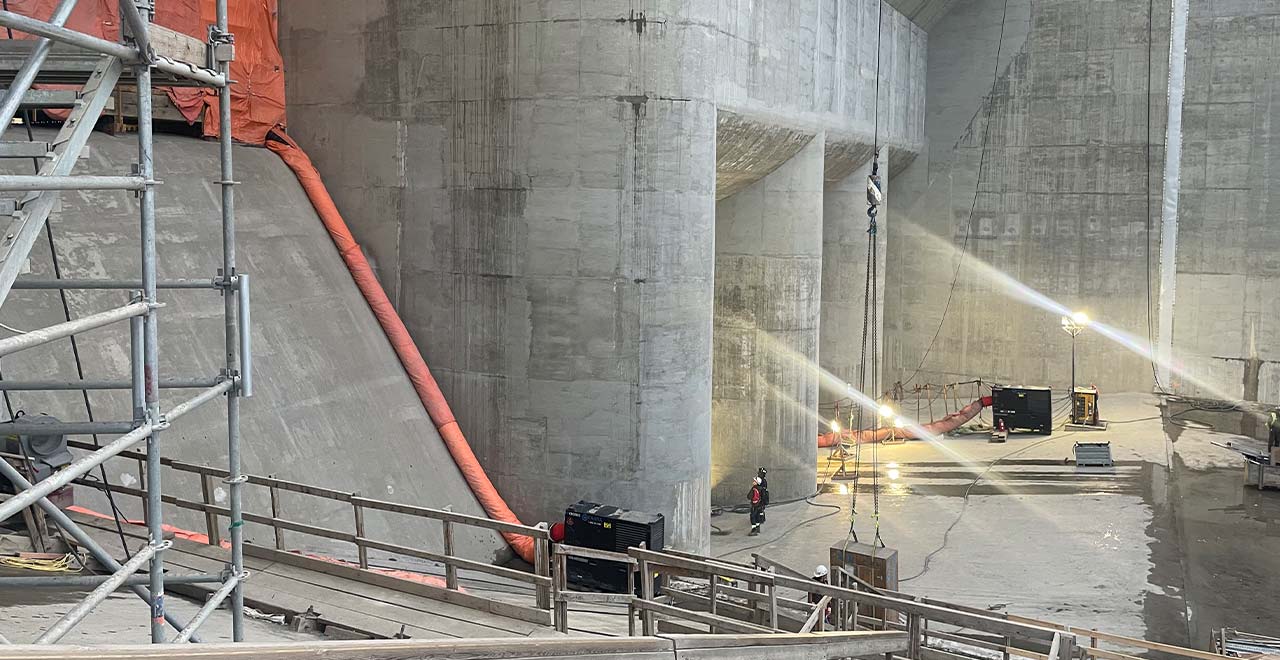 Heavy construction equipment and scaffolding at a large concrete tunnel site under construction.
